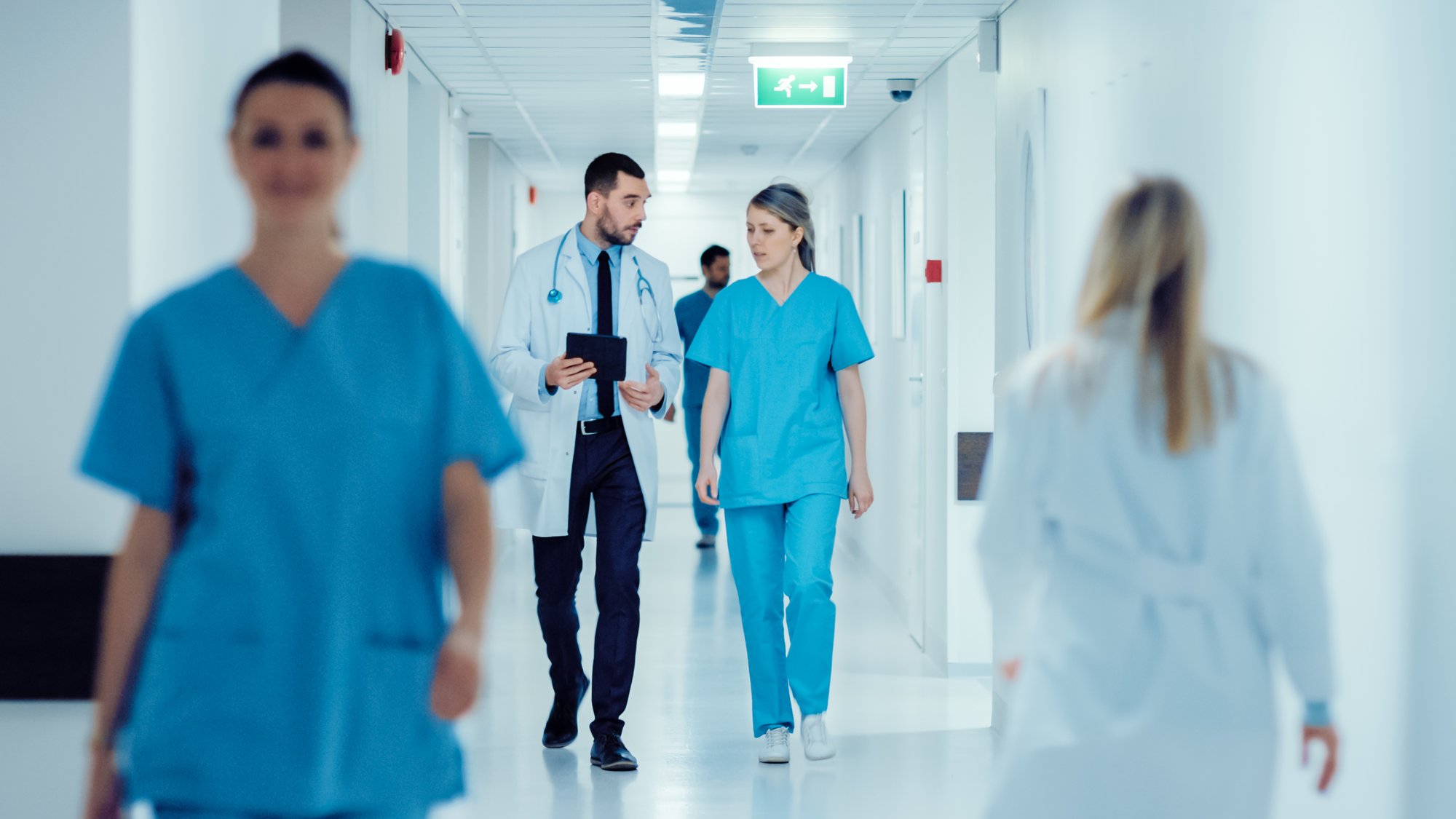 Doctors and nurses walk and talk in a brightly lit hospital hallway, representing a busy healthcare environment focused on patient care and safety. Doctors and nurses walk and talk in a brightly lit hospital hallway, representing a busy healthcare environment focused on patient care and safety.