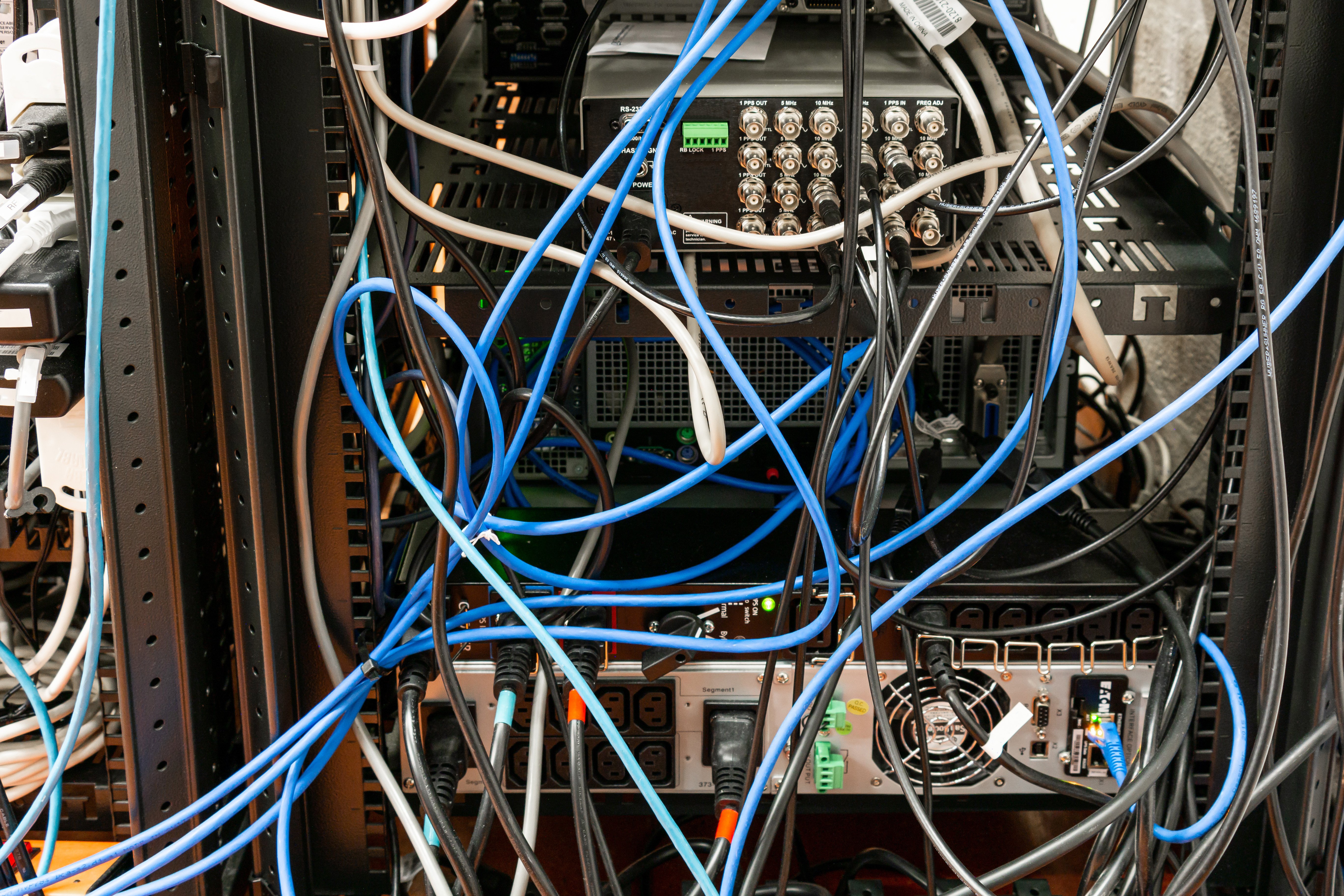Messy network closet with tangled blue, gray, and white cables connected to networking equipmen