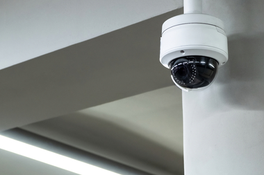 A security camera mounted on a ceiling monitors an indoor area, representing modern video surveillance for workplace safety and incident prevention.