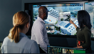 A security operations team reviews live video feeds and facility layouts on a large digital display, coordinating safety and surveillance across a connected campus.