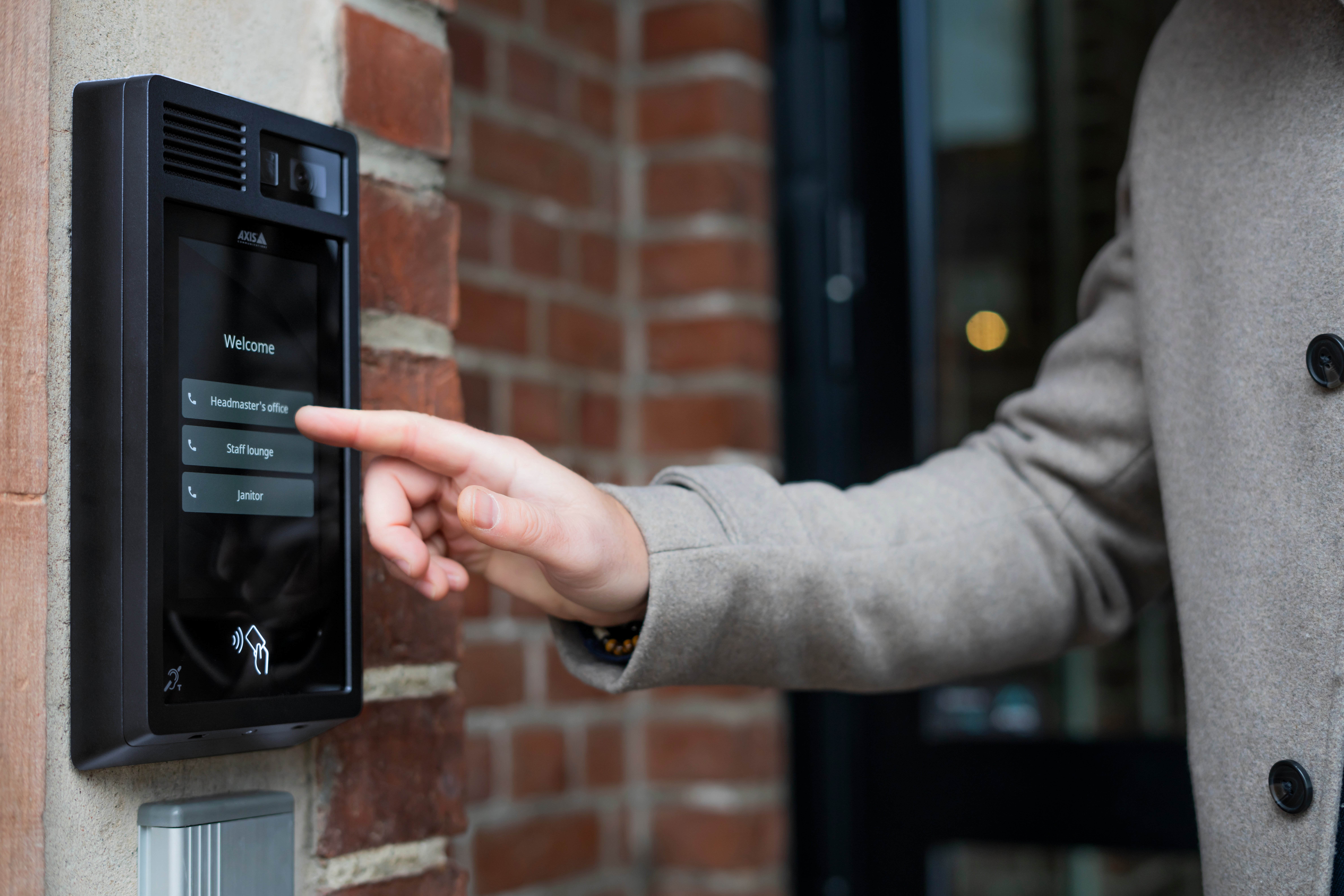 Person using a video intercom mounted on a brick wall outside a building entrance.
