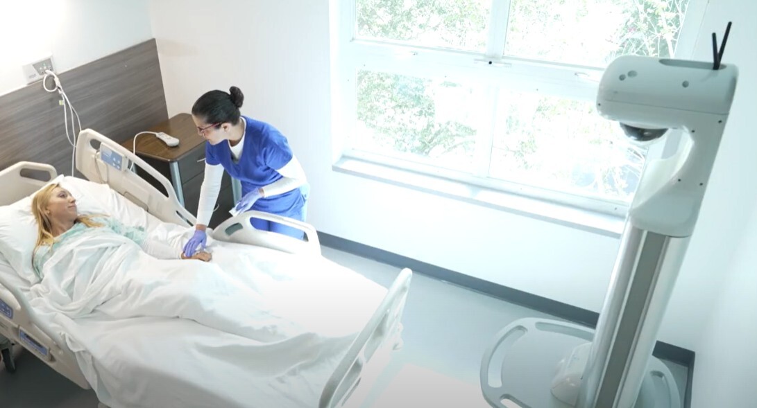 Hospital room with a patient in bed and a healthcare worker in blue scrubs attending to them Hospital room with a patient in bed and a healthcare worker in blue scrubs attending to them